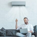 Video - 4 Amazing Benefits of Ductless Units. Man sitting on his couch with his laptop and holding remote to his ductless system on the wall.